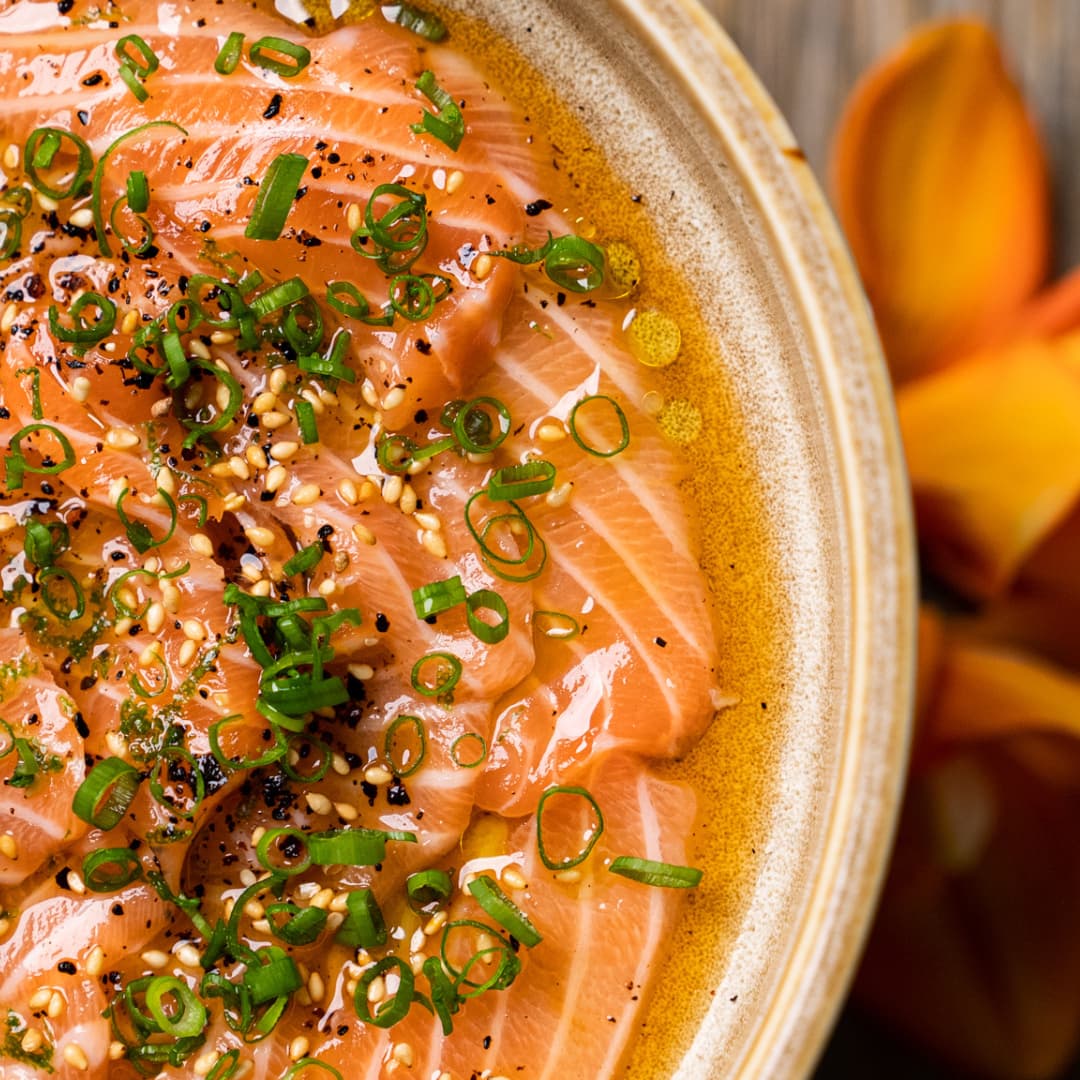 Close-up of salmon carpaccio with sesame seeds and spring onion in a handmade ceramic bowl