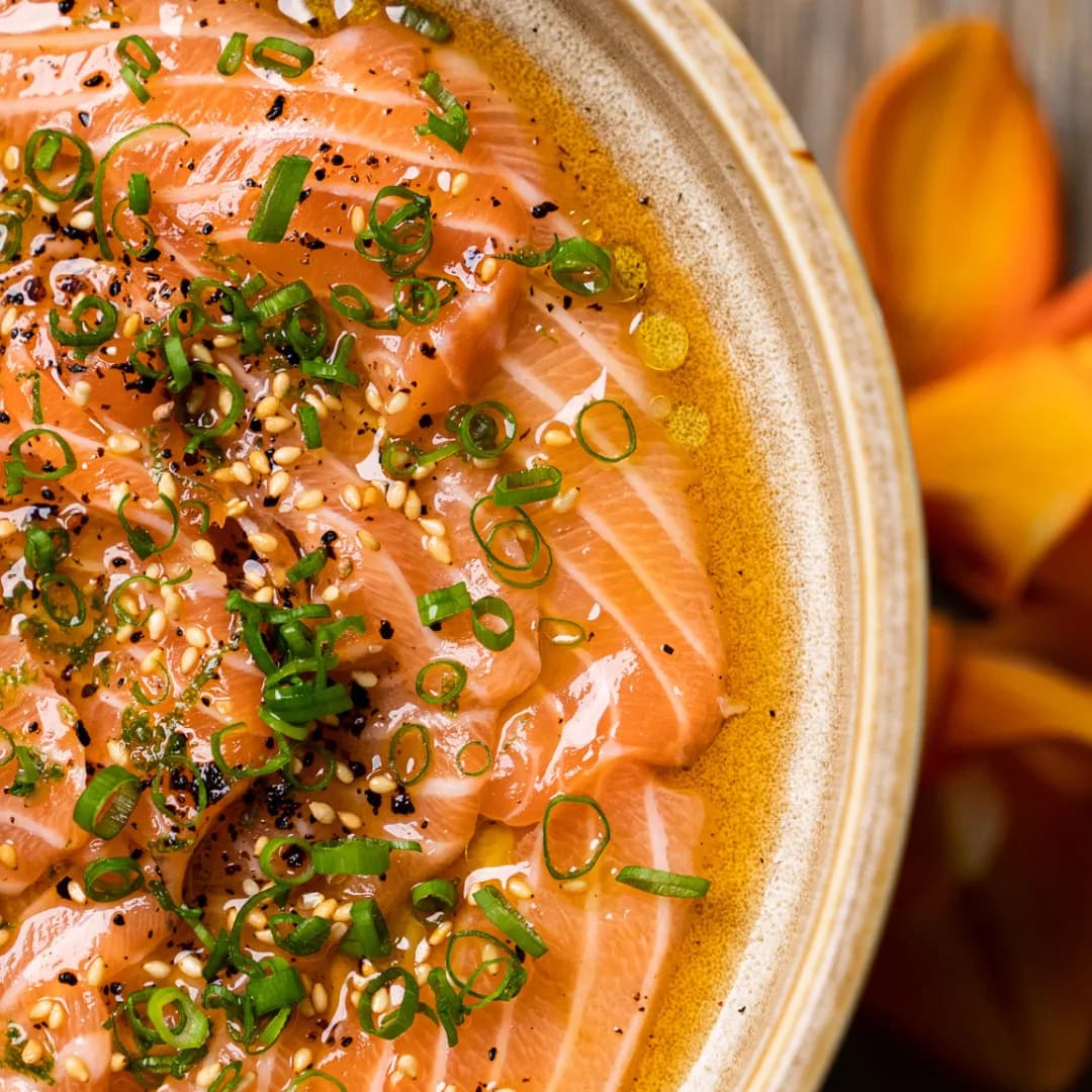 Close-up of salmon carpaccio with sesame seeds and spring onion in a handmade ceramic bowl