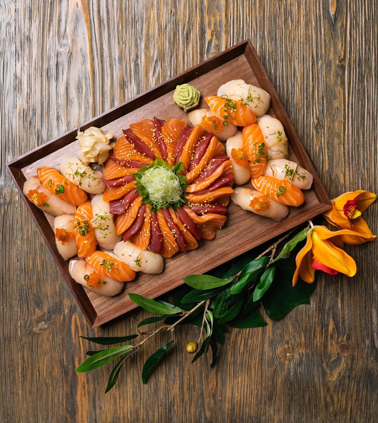 Artfully arranged sashimi platter — salmon, tuna, scallop — on a rustic wooden board with wasabi and ginger